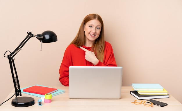 Jonge studentenvrouw op een werkplaats met laptop die aan de kant richten om een product te presenteren