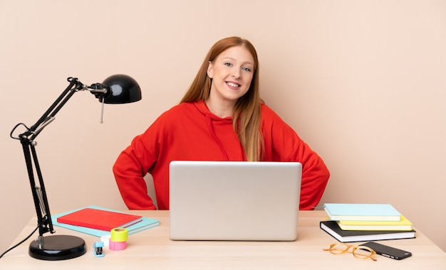 Jonge studentenvrouw op een werkplaats met laptop het stellen met wapens bij heup en het glimlachen