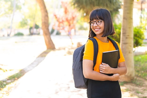 Jonge studentenvrouw wint een park met een notitieboekje met een vrolijke uitdrukking