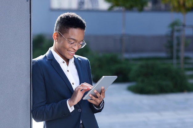 Jonge succesvolle Afro-Amerikaanse zakenvrouw in de buurt van het kantoor gebruikt een tabletcomputer, gelukkige vrouwelijke student glimlacht en geniet van online leren