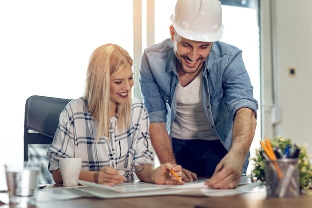 Foto jonge succesvolle architectencollega's die blauwdrukken bespreken en analyseren terwijl ze aan een nieuw project op kantoor werken.