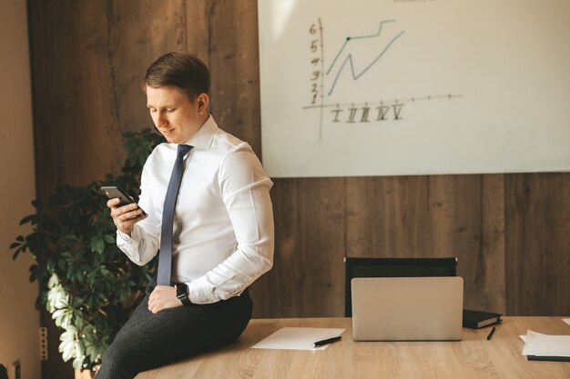 Jonge succesvolle mannelijke zakenman die een smartphone in zijn handen houdt. Communicatietechnologieën.