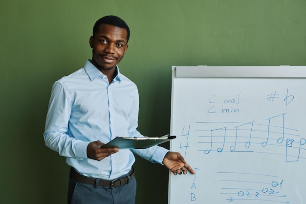 Jonge succesvolle muziekleraar met document wijzend op whiteboard met muzieknoten tijdens exp