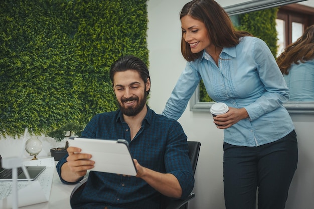 Jonge succesvolle ontwerpers werken aan een digitale tablet en praten over een project op kantoor tijdens de koffiepauze.