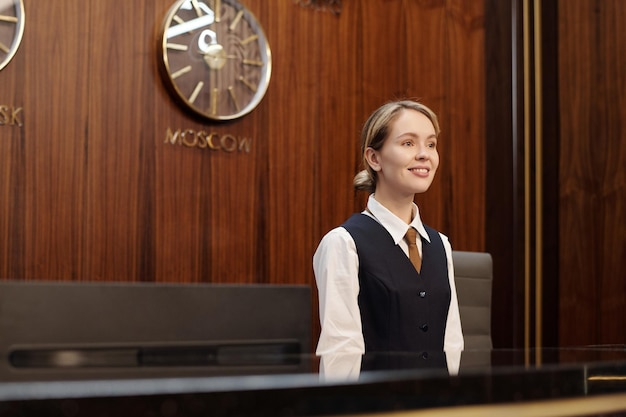 Foto jonge succesvolle vrouwelijke receptioniste in uniform die bij de balie staat