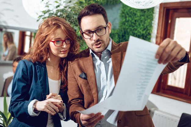 Jonge succesvolle zakencollega's die project analyseren, papierwerk bekijken en erover praten op kantoor.