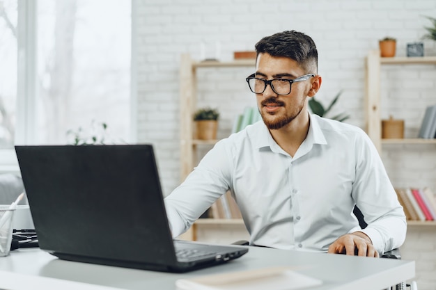 Jonge succesvolle zakenman met behulp van laptop op zijn bureau