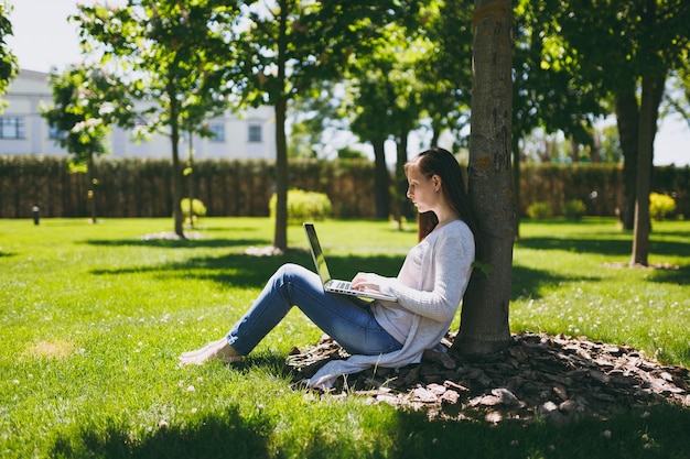 Jonge succesvolle zakenvrouw in casual kleding. vrouw zitten op gras grond, werken op laptop pc-computer in stadspark op groen gazon buiten op de natuur. mobiel kantoor. freelance bedrijfsconcept.
