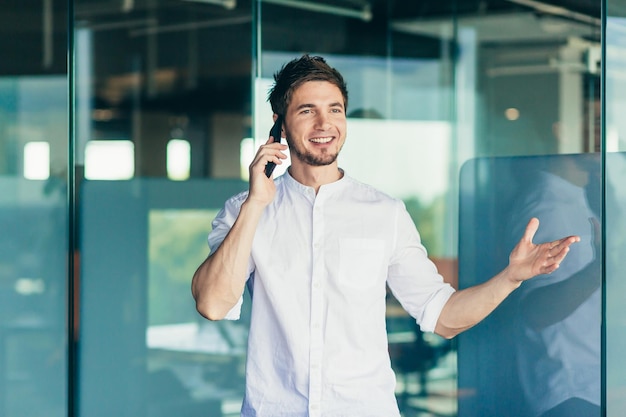 Jonge succesvolle zakenvrouw praten bij het raam op kantoor aan de telefoon man glimlachend en gekleed in een shirt