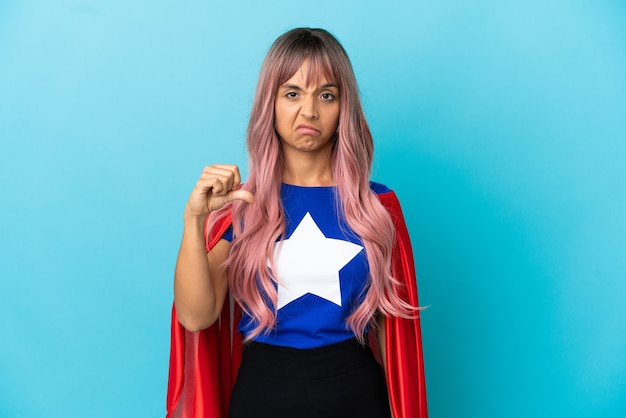 Jonge superheld vrouw met roze haren geïsoleerd op een blauwe achtergrond met duim omlaag met negatieve expressie