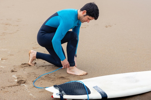 Jonge surfer aan de kust die zijn surfplank vastbindt aan zijn enkel.