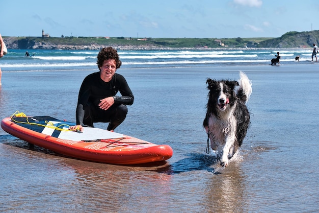 Jonge surfer met lang krullend haar die met zijn border collie-hond poseert terwijl hij rent