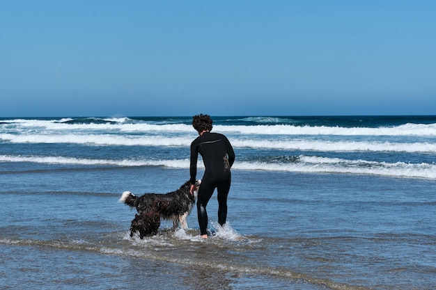 Jonge surferjongen die met zijn border collie-hond aan zee speelt