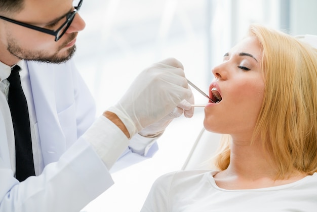 Foto jonge tandarts die patiënt in tandkliniek onderzoeken.