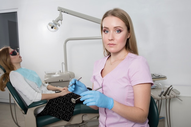 Jonge tandarts meisje met een medisch instrument tegen de achtergrond van een tandartspraktijk