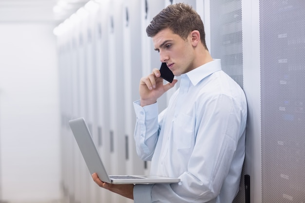 Jonge technicus die en zijn notitieboekje telefoneert gebruikt