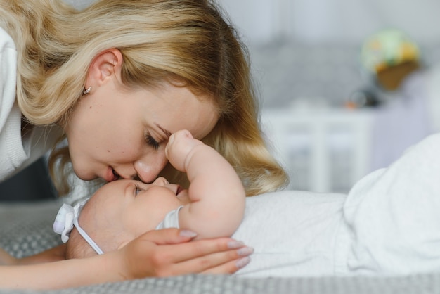 Jonge tedere gelukkige moeder knuffelen haar pasgeboren baby glimlachend zittend op bed in de ochtend.