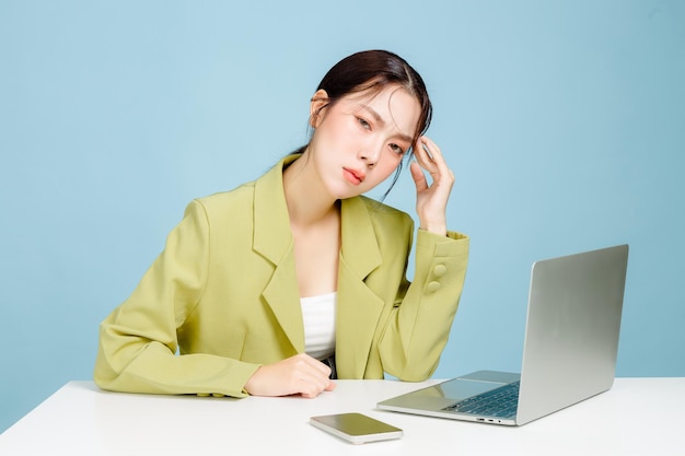Jonge teleurgestelde onrustige verwarde werknemer zakenvrouw in casual pak zit aan een wit bureau met laptop en gebruikt mobiele telefoon op pastelblauwe achtergrond
