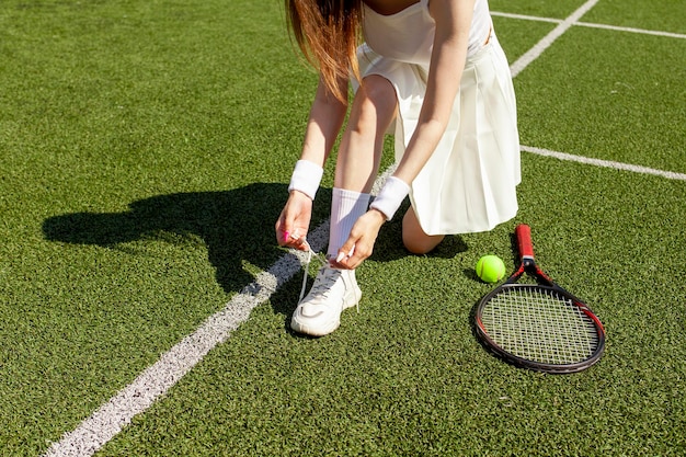 Foto jonge tennisspeler in wit sportuniform bindt haar schoenveters aan sneakers op het groene veld
