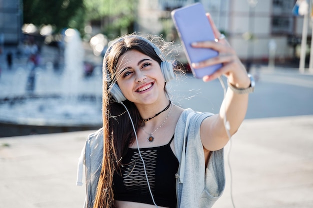 Jonge tiener die een selfie maakt met een vrouw van een mobiele telefoon met een koptelefoon die een videogesprek voert in de stad