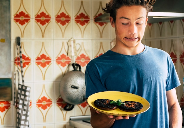 Jonge tiener met verbrande te gekookte hamgurger met grappige uitdrukking in de keuken