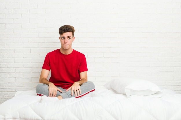 Jonge tiener student man op het bed in de war, voelt zich twijfelachtig en onzeker.