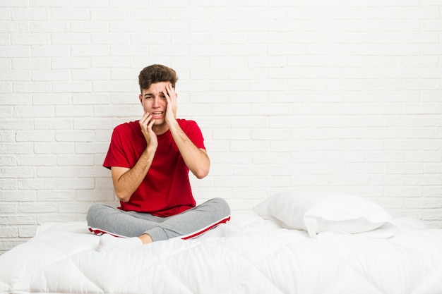 Jonge tiener student man op het bed zeuren en troosteloos huilen.