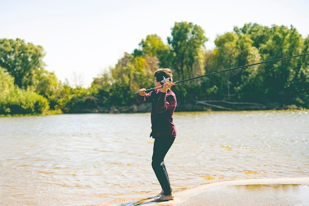 jonge tiener visser in casual vis vangen op de rivieroever met rod op een zomerdag