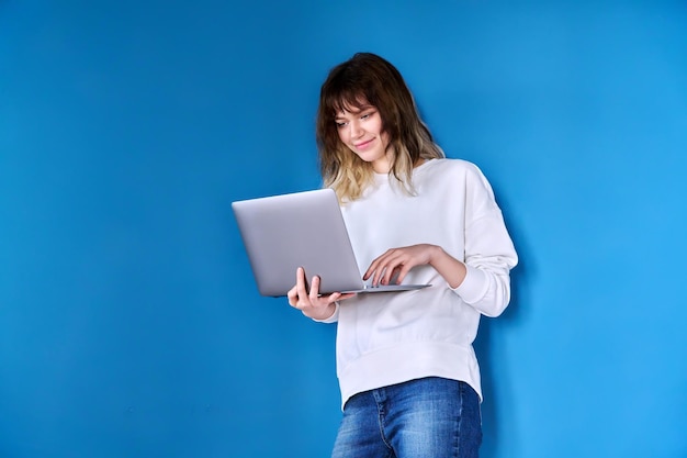 Jonge tiener vrouw met laptop op blauwe achtergrond