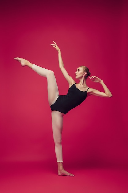 Foto jonge tienerdanser die op rode studioachtergrond danst. ballerinaproject met kaukasisch model. het concept van ballet, dans, kunst, hedendaags choreografie