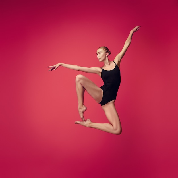 Jonge tienerdanser die op rode studioachtergrond danst. Ballerinaproject met Kaukasisch model. Het concept van ballet, dans, kunst, hedendaags choreografie