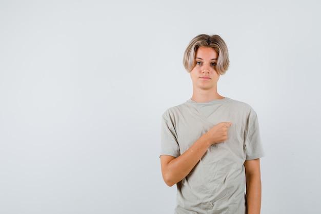 Jonge tienerjongen die gebalde vuist op de borst houdt in een t-shirt en er trots uitziet. vooraanzicht.