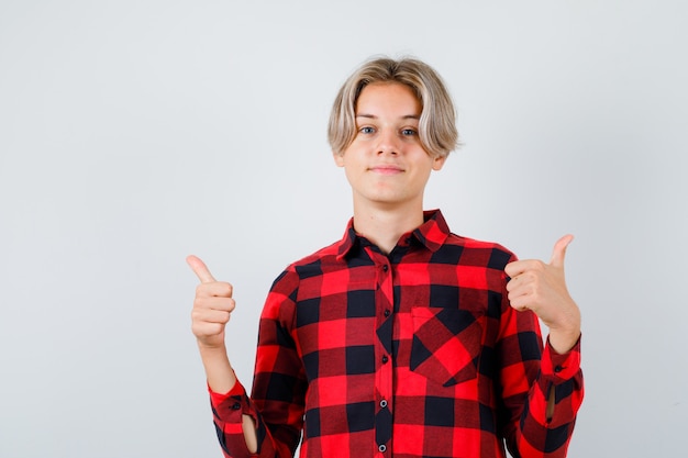 Jonge tienerjongen in geruit hemd die duimen laat zien en er tevreden uitziet, vooraanzicht.