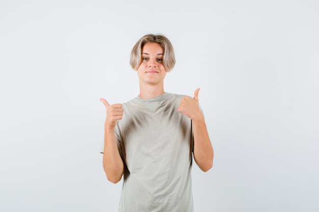 Jonge tienerjongen in t-shirt die dubbele duimen toont en er trots uitziet, vooraanzicht.