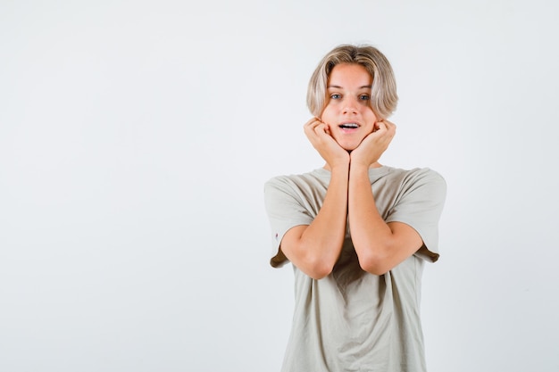 Jonge tienerjongen in t-shirt die zijn gezicht op zijn handen dempt en zich afvroeg?