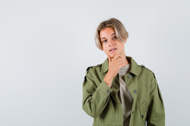 Jonge tienerjongen met hand op kin in groen jasje en zelfverzekerd kijkend