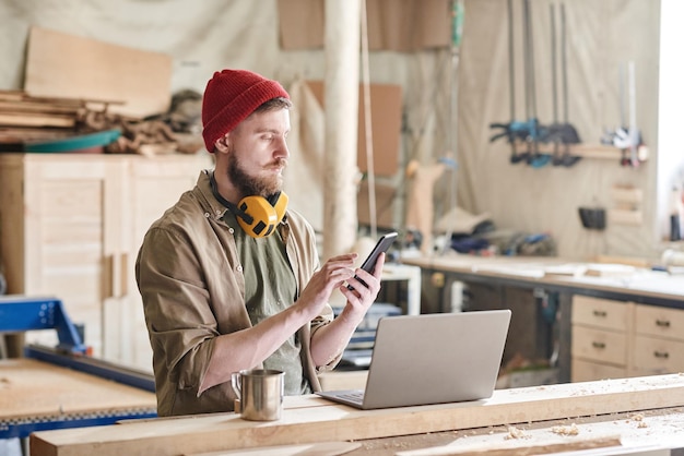 Foto jonge timmerman met smartphone in werkplaats