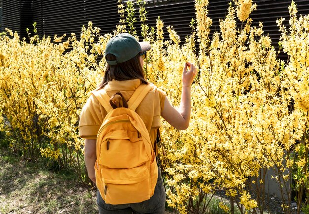 Foto jonge toeriste in pet met gele rugzak tussen bloeiende forsythia struiken die takken raken in de lente of zomer geniet van de natuur persoon