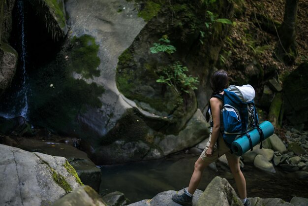 jonge toeristenvrouw in bos dichtbij waterval met rugzak