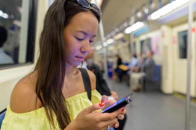 Jonge toeristische vrouw met behulp van telefoon bij metro trein in Bangkok