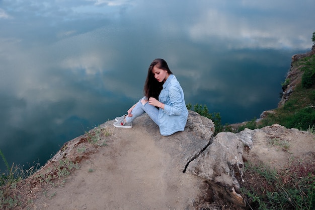 Jonge toeristische vrouw zit op de top van de montage en kijkt naar een prachtig landschap. Wandelende vrouw ontspannen op de top van de klif genieten van. aantrekkelijk meisje in spijkerkleding