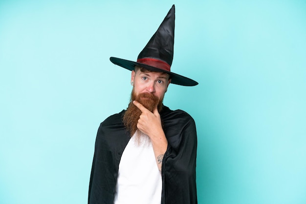 Foto jonge tovenaar in halloween geïsoleerd op blauwe achtergrond denken