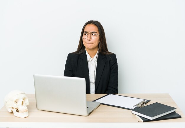 Jonge traumatoloog Aziatische vrouw geïsoleerd op witte muur verward, twijfelachtig en onzeker.