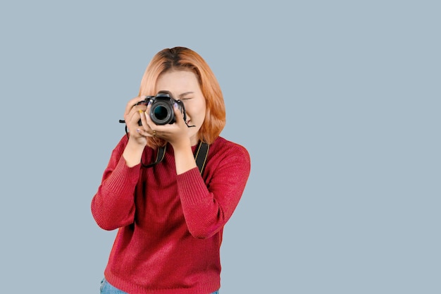 Jonge trendy fotograaf met rood haar maakt een foto op geïsoleerde grijze achtergrond