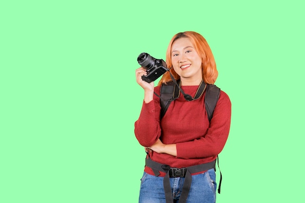 Jonge trendy fotograaf met rood haar met camerarugzak die zich op geïsoleerde groene achtergrond bevindt