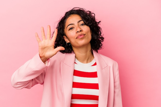 Jonge trendy Latijns-vrouw geïsoleerd op roze achtergrond glimlachend vrolijk weergegeven: nummer vijf met vingers.