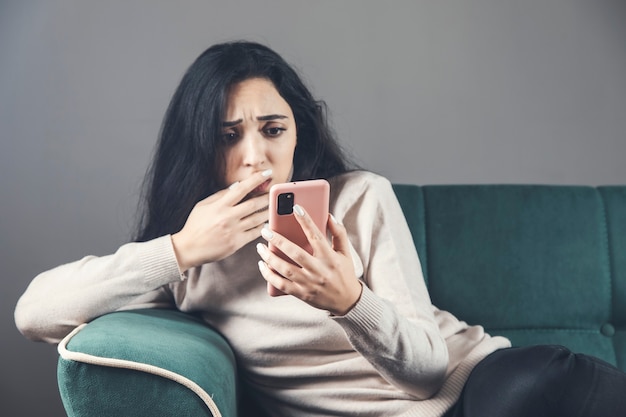 Jonge triest vrouw zittend op de Bank met behulp van smartphone