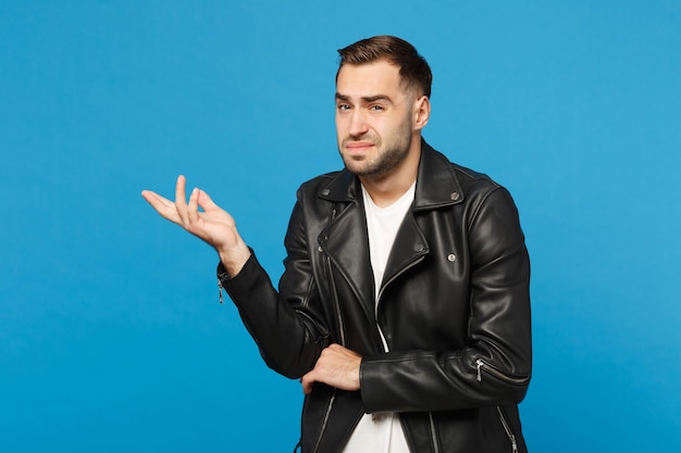 Jonge trieste gefrustreerde bezorgde ongeschoren man in zwarte jas wit t-shirt op zoek camera geïsoleerd op blauwe muur achtergrond studio portret. mensen oprechte emoties levensstijl concept. bespotten kopie ruimte.