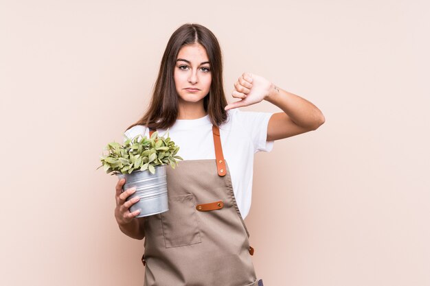 Jonge tuinman blanke vrouw met een plant geïsoleerd met een afkeer gebaar, duimen naar beneden. Meningsverschil concept.