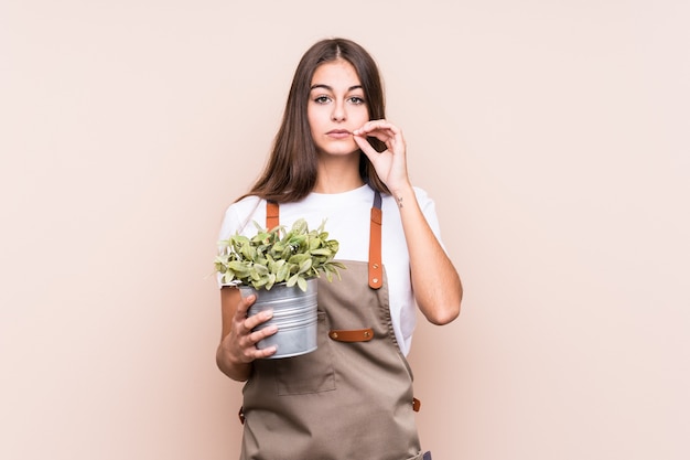 Jonge tuinman blanke vrouw met een plant isolatedwith vingers op lippen houden een geheim.